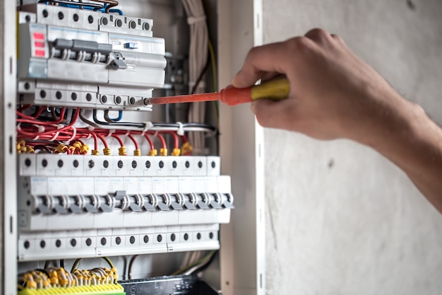 Mann, ein Elektrotechniker, der in einer Schalttafel mit Sicherungen arbeitet. Installation und Anschluss von elektrischen Geräten. Nahansicht.