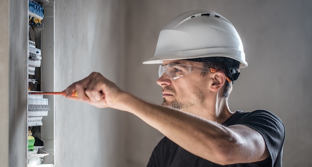 Mann, ein Elektrotechniker, der in einer Schalttafel mit Sicherungen arbeitet. Installation und Anschluss von elektrischen Geräten.