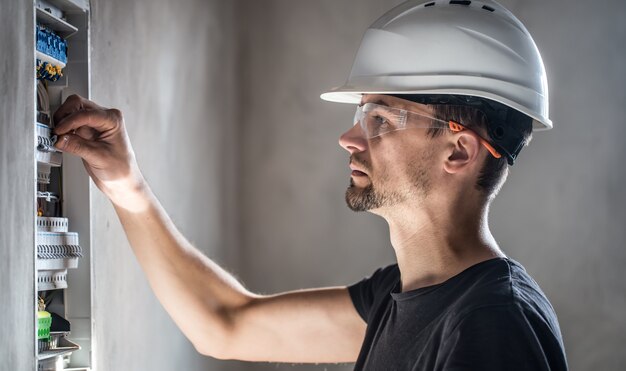 Mann, ein Elektrotechniker, der in einer Schalttafel mit Sicherungen arbeitet. Installation und Anschluss von elektrischen Geräten.