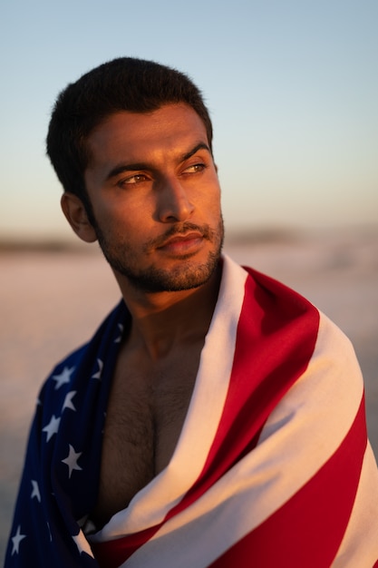Mann eingewickelt in der amerikanischen Flagge, die auf dem Strand steht