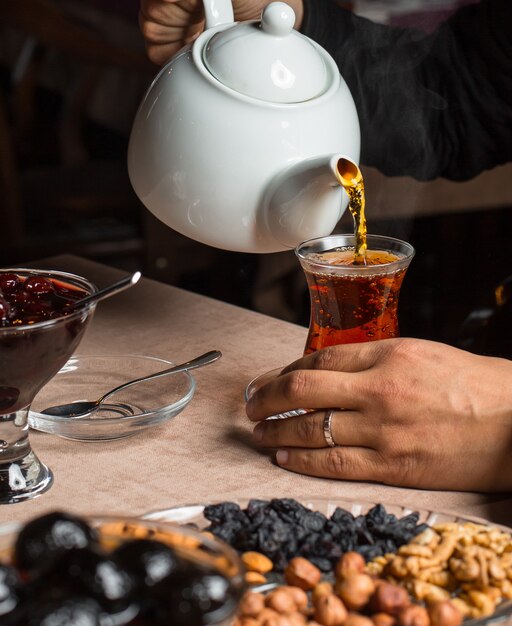 Mann gießt schwarzen Tee aus der Teekanne, serviert mit getrockneten Früchten, Marmelade