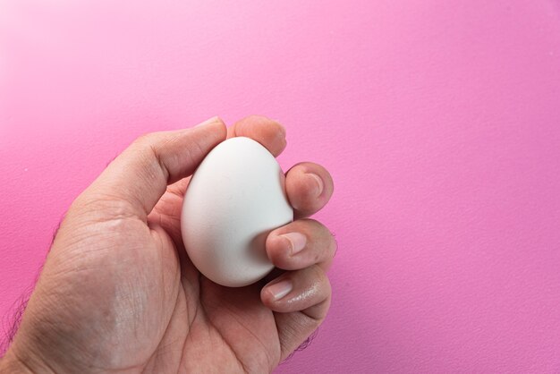 Mann hält Ei über rosa Hintergrund