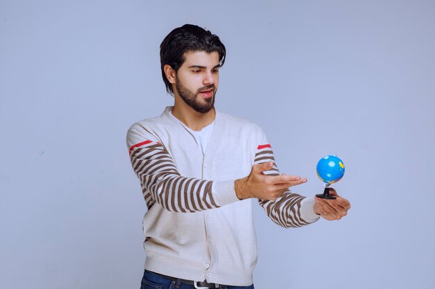 Mann hält einen Mini-Globus, schüttelt ihn und versucht, einen Ort zu erraten.