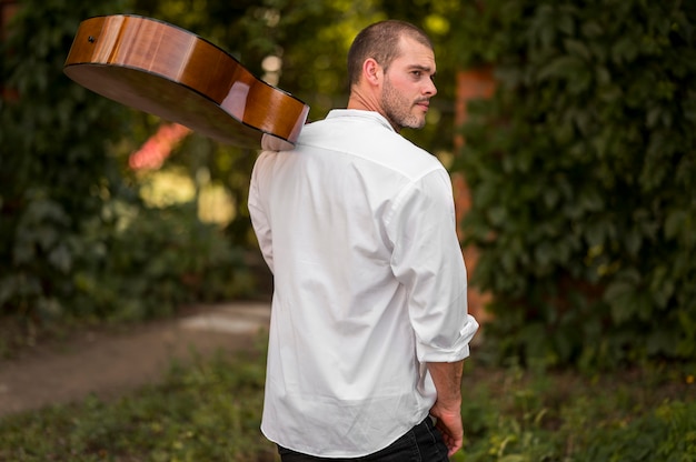 Kostenloses Foto mann hält seine gitarre auf der schulter von hinten schuss