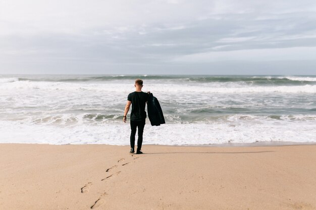Mann hält seine Jacke am Strand