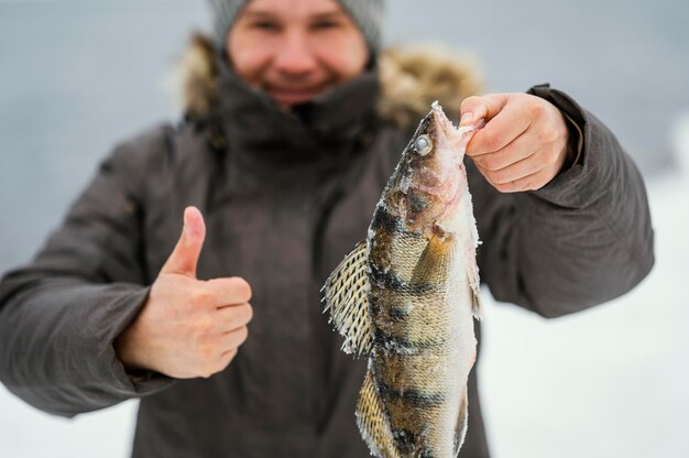 Mann hält siegreich einen Fisch, den er gefangen hat