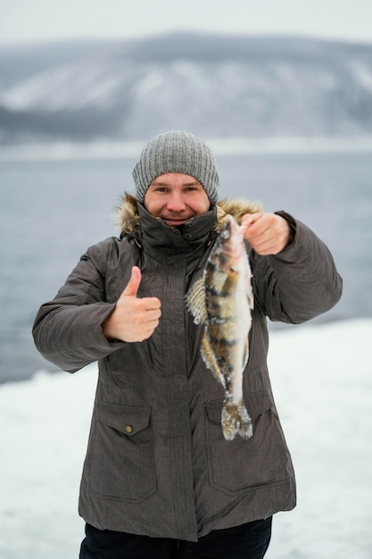 Mann hält siegreich einen Fisch, den er gefangen hat