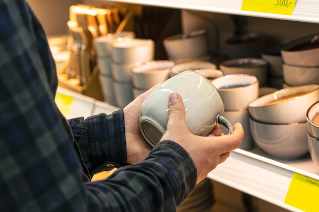 Kostenloses Foto mann hält tasse aus einem regal im haushaltswarenladen