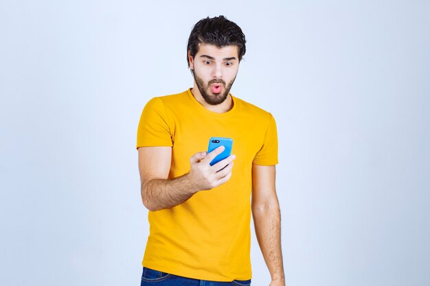 Mann im gelben Hemd, das ein blaues Smartphone hält.