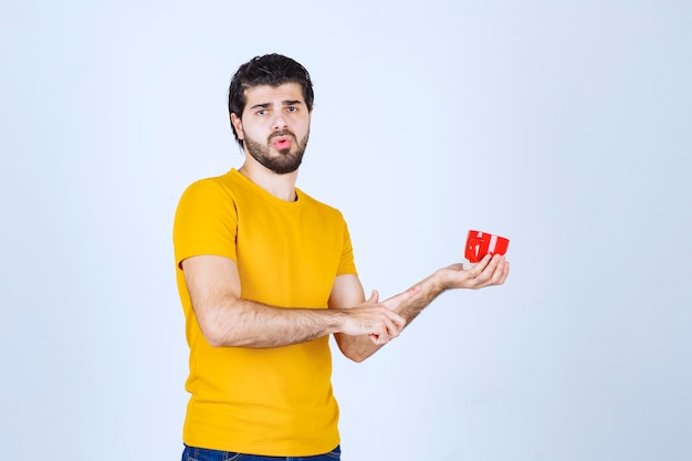 Mann im gelben Hemd, das eine rote Tasse hält und denkt.