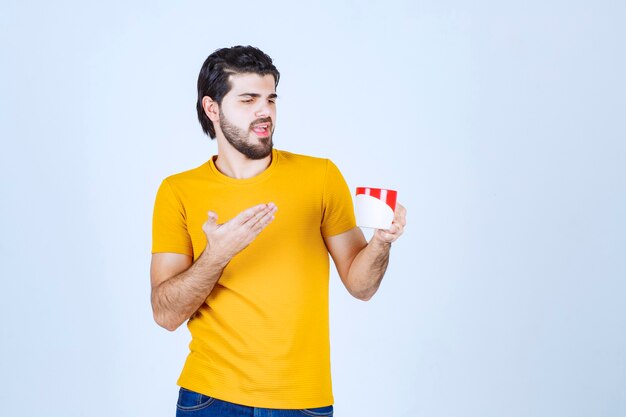 Mann im gelben Hemd, das eine rote Tasse hält und denkt.