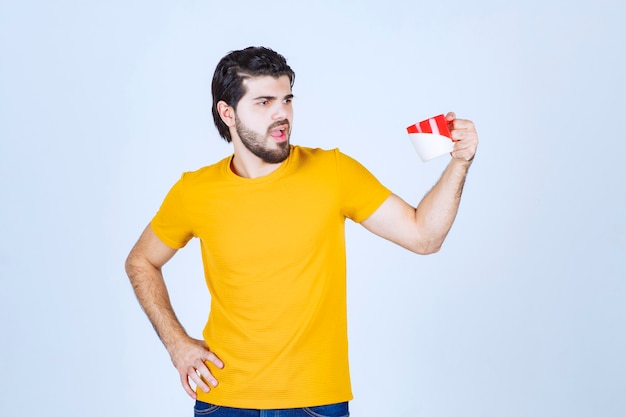 Mann im gelben Hemd, das eine rote Tasse hält und denkt.