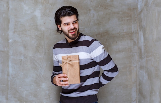 Mann im gestreiften Hemd hält eine Geschenkbox aus Karton und lächelt