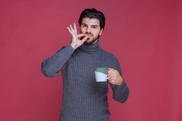 Mann im grauen Pullover, der eine Kaffeetasse hält und den Geschmack genießt.