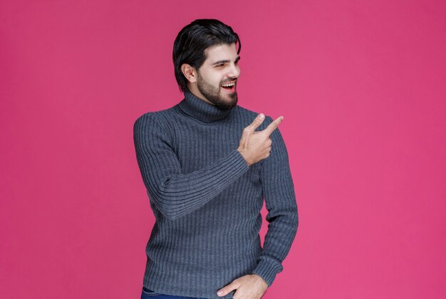 Mann im grauen Pullover, der etwas zeigt oder jemanden mit dem Zeigefinger vorstellt.