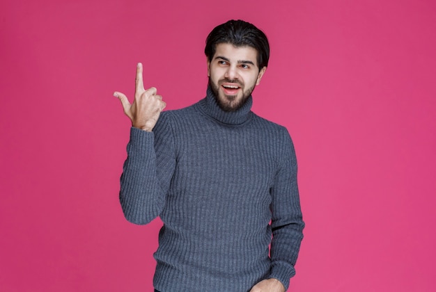 Mann im grauen Pullover, der etwas zeigt oder jemanden mit dem Zeigefinger vorstellt.
