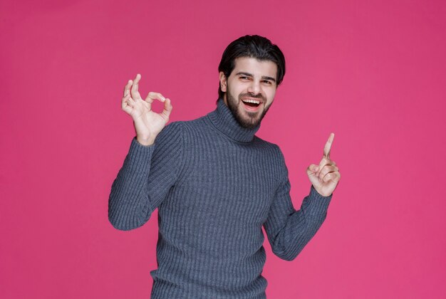 Mann im grauen Pullover, der etwas zeigt oder jemanden mit dem Zeigefinger vorstellt.