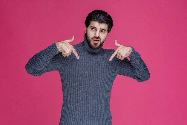 Mann im grauen Pullover, der sich mit dem Zeigefinger zeigt.