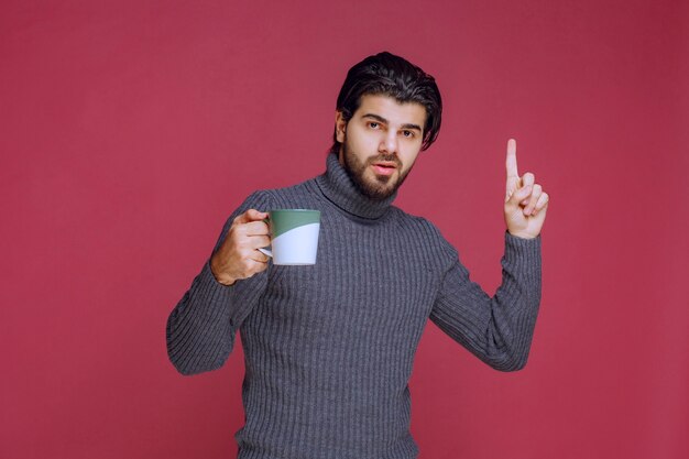 Mann im grauen Pullover hält einen Becher und bittet um Aufmerksamkeit.