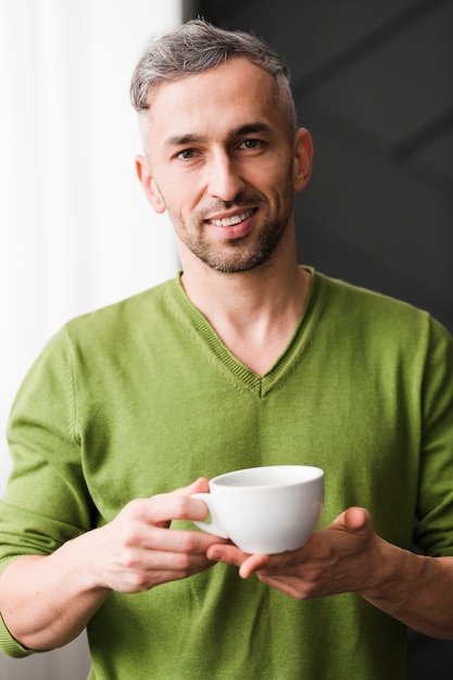 Mann im grünen Hemd, das einen weißen Tasse Kaffee hält