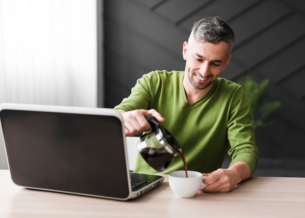 Mann im grünen Hemd mit Laptop und Kaffee