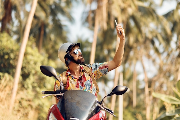 Mann im helm sitzt auf motorrad und benutzt handy