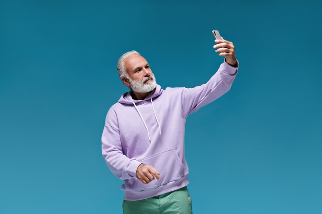 Mann im Hoodie macht Selfie an blauer Wand