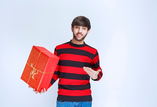 Mann im rot gestreiften Hemd, das eine rote Geschenkbox hält und sie fördert.