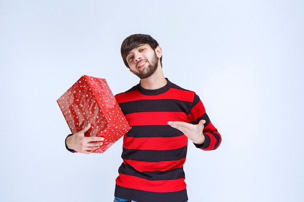 Mann im rot gestreiften Hemd, das eine rote Geschenkbox hält und sie fördert.