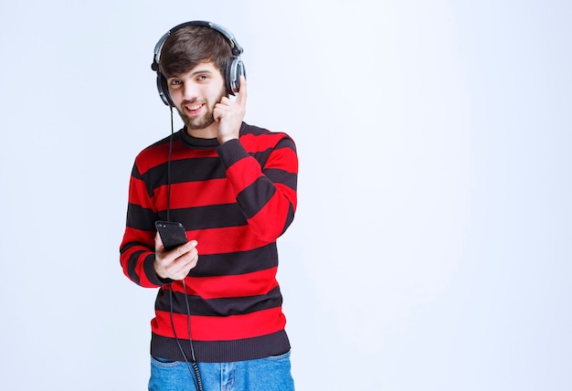 Mann im rot gestreiften hemd, das kopfhörer hört und musik aus seiner playlist auf dem smartphone einstellt.