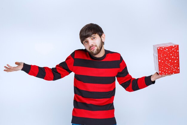 Mann im rot gestreiften Hemd mit roter Geschenkbox sieht verwirrt und nachdenklich aus.