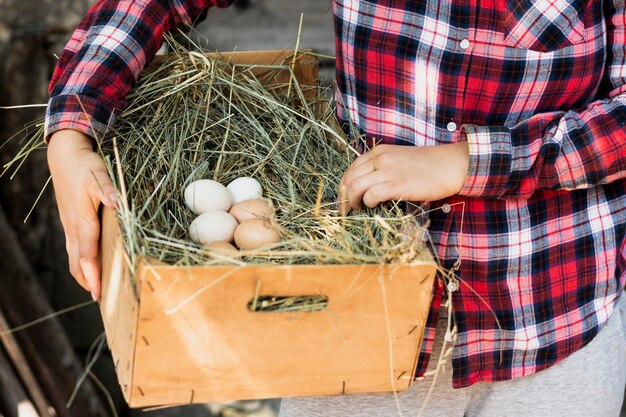 Mann im roten quadratischen Hemd, das einen Kasten mit einem Nest mit Eiern hält