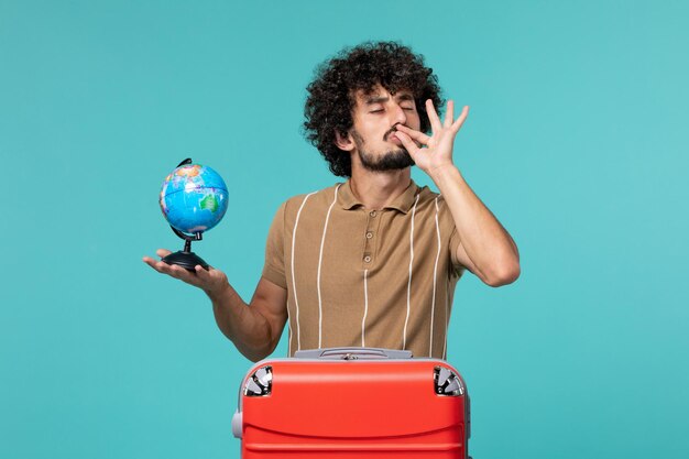 Mann im Urlaub, der kleine Kugel mit roter Tasche auf blauem Boden hält Reise Urlaub Flugzeug Reise Seereise