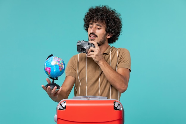 Mann im Urlaub hält kleinen Globus und Kamera auf Blau