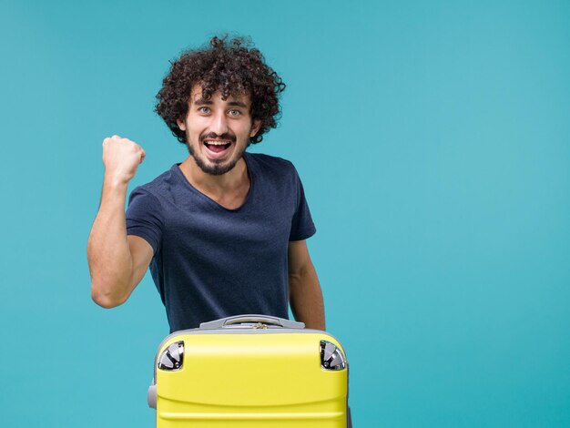 Mann im Urlaub mit gelbem Koffer, der sich auf Blau glücklich fühlt