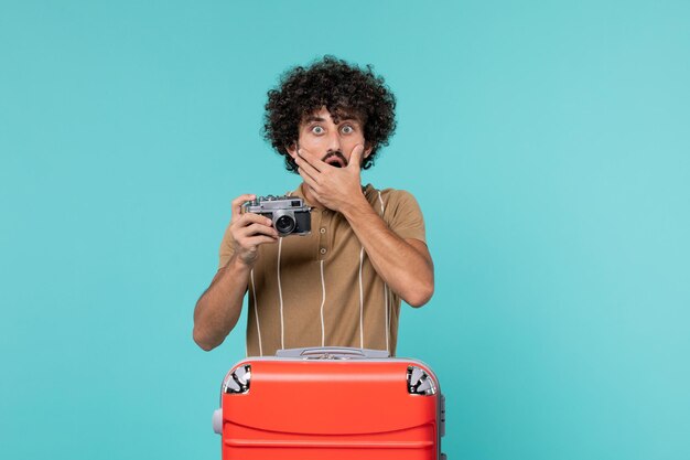 Mann im Urlaub mit rotem Koffer, der Fotos mit Kamera auf Blau macht