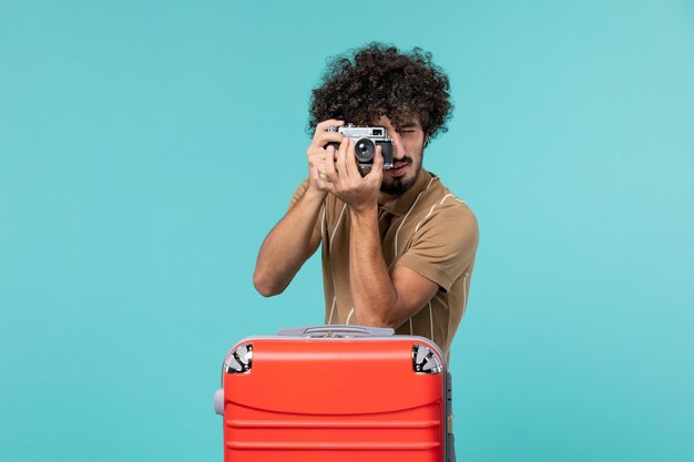Mann im Urlaub mit rotem Koffer, der Fotos mit Kamera auf Blau macht