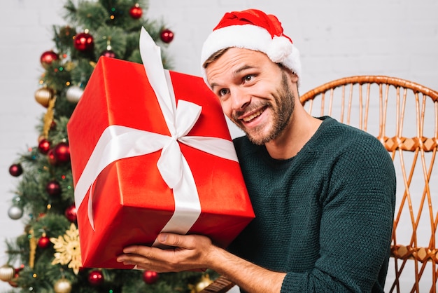 Kostenloses Foto mann im weihnachtshut, der präsentkarton hält