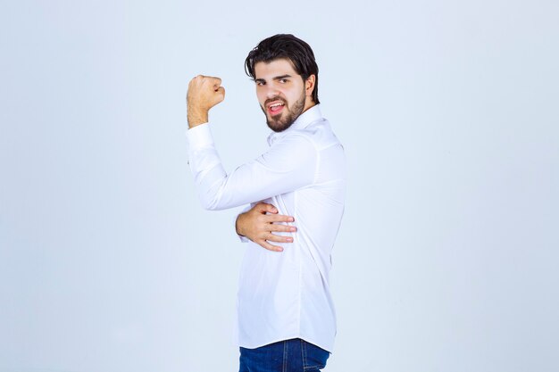 Mann im weißen Hemd, das seine Armmuskeln und Faust zeigt.