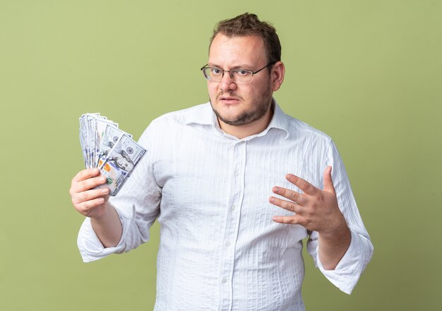 Mann im weißen Hemd mit Brille, der Bargeld in der Hand hält und verwirrt und sehr ängstlich aussieht