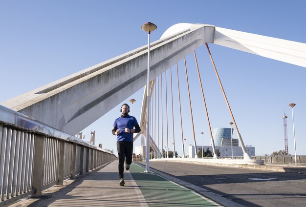 Mann in blauen Kopfhörern mit seinem Handy beim Joggen auf der Straße