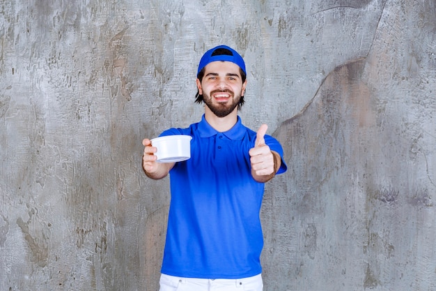 Mann in blauer Uniform, der einen Plastikbecher zum Mitnehmen hält und ein positives Handzeichen zeigt.
