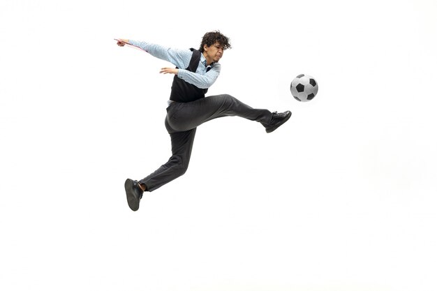 Mann in Bürokleidung, die Fußball oder Fußball mit Ball auf weißem Raum spielt. Ungewöhnlicher Blick für Geschäftsmann in Bewegung, Aktion. Sport, gesunder Lebensstil.