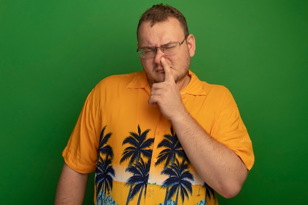 Mann in den Gläsern und in der orangefarbenen Hemdschließnase mit dem verwirrten Finger, der über grüner Wand steht