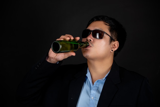 Mann in dunkler Jacke und Sonnenbrille trinkt eine Bierflasche
