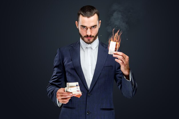 Mann in einem Anzug, der brennendes Bargeld und Bankkarte hält. isoliert auf grauem Hintergrund.