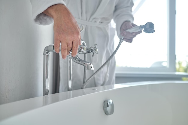 Mann in einem weißen Frottee-Bademantel, der die Badewanne mit Wasser füllt