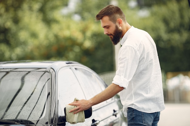 Mann in einem weißen Hemd wischt ein Auto in einer Autowäsche ab