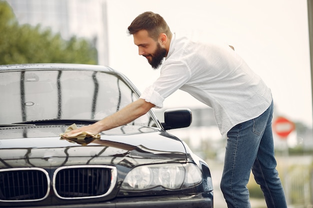 Mann in einem weißen Hemd wischt ein Auto in einer Autowäsche ab