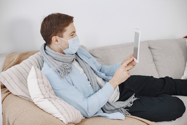 Mann in einer medizinischen Maske. Mann, der zu Hause im Wohnzimmer sitzt. Kerl, der es genießt, in Quarantäne zu lernen.